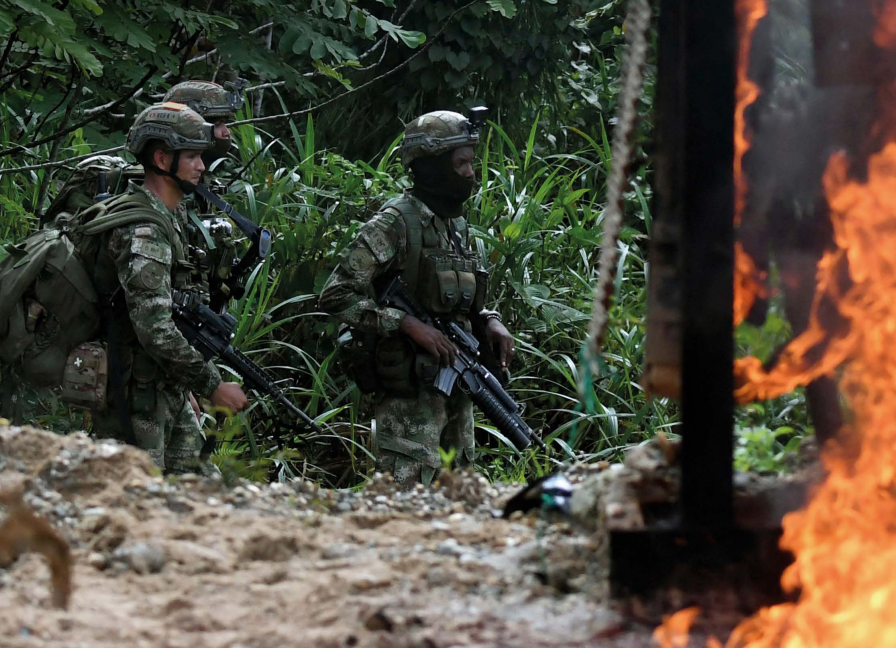 : Police officers and soldiers stand next to destroyed heavy machinery used on an illegal gold mine in Triangulo de Telembi, Colombia.